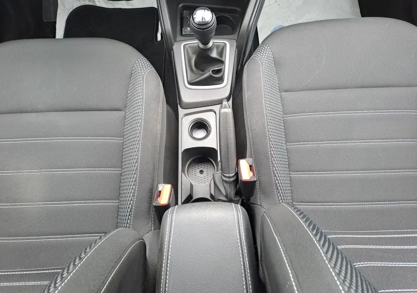Vue intérieure centrée sur la console centrale et les sièges avant en tissu noir du Dacia Duster 2024 avec boîte manuelle.