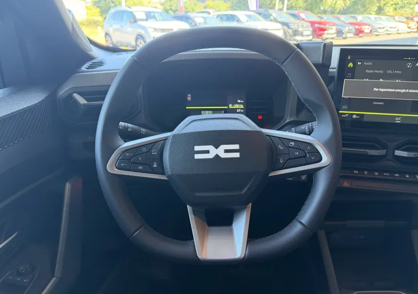 Vue intérieure centrée sur le volant noir du Dacia Duster Hybrid 155 Journey avec tableau de bord et écran tactile.
