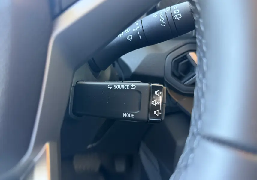 Gros plan sur la commande multimédia au volant du Dacia Duster Hybrid 155 Journey noir, avec indications source et mode.