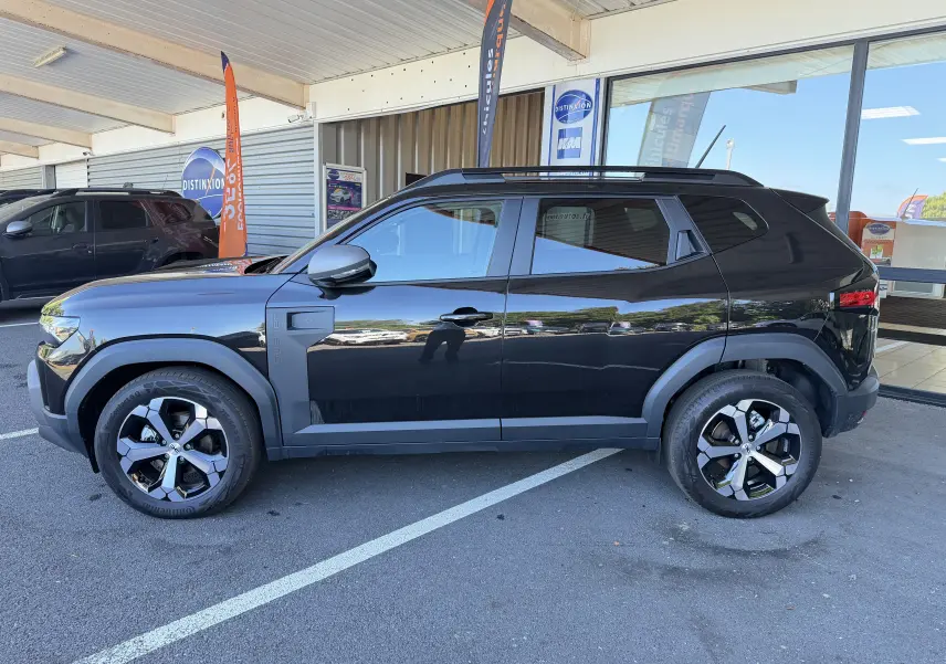 Vue de profil côté gauche d'un Dacia Duster Hybrid 155 Journey noir avec jantes alliage 18 et barres de toit.