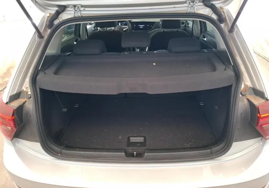 Coffre ouvert d'une Volkswagen Polo gris clair vue de l'arrière, avec tablette cache-bagages et intérieur sombre visible.
