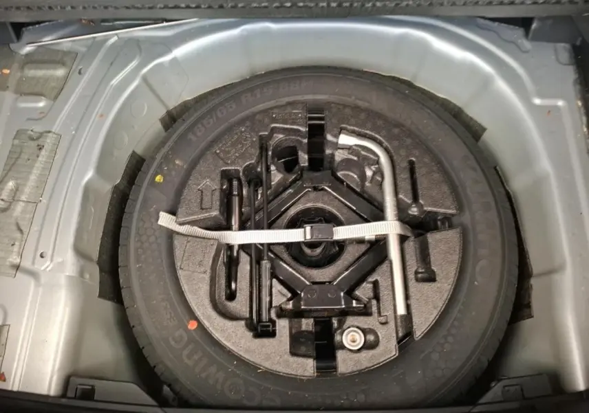 Vue plongeante sur la roue de secours acier 15 pouces et outillage de bord dans le coffre d'une Volkswagen Polo gris clair.
