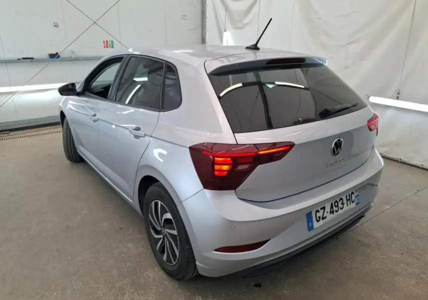 Volkswagen Polo gris clair vue 3/4 arrière droit avec feux arrière allumés dans un garage.
