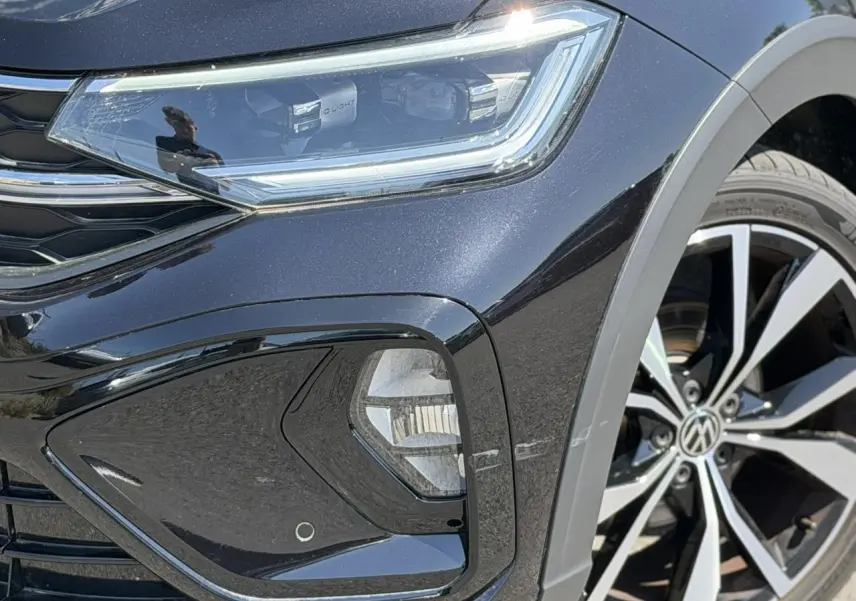 Gros plan sur l'avant droit noir métallisé du Volkswagen Taigo R-Line, mettant en valeur le phare Matrix LED et la jante 18 pouces.