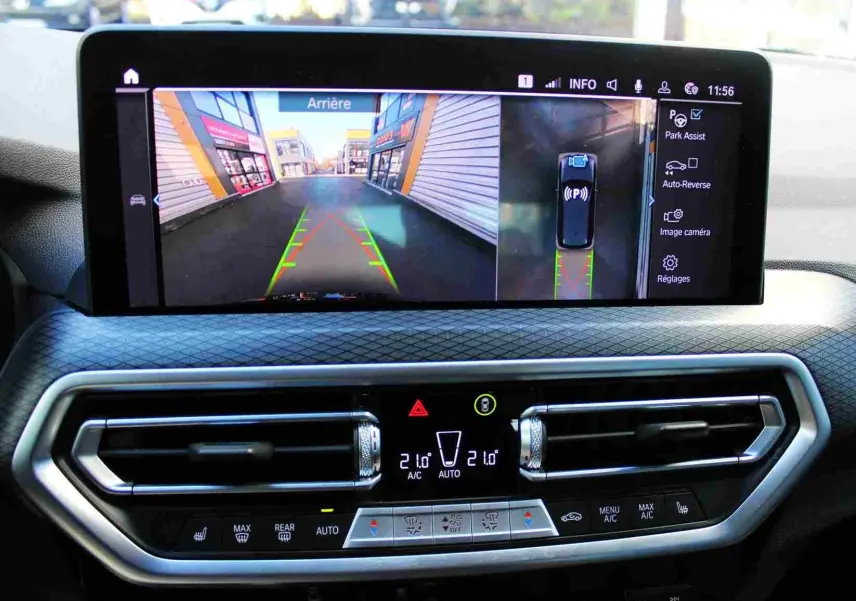 Vue intérieure du tableau de bord du BMW X3 xDrive 30e 2023 avec écran d'aide au stationnement et commandes climatisation.