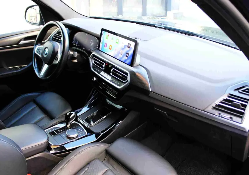 Intérieur BMW X3 xDrive 30e 2023, vue côté conducteur sur tableau de bord moderne avec écran tactile et cuir noir.