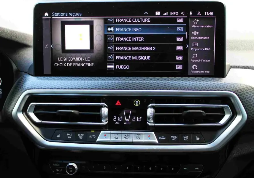 Tableau de bord du BMW X3 xDrive 30e 2023 avec écran tactile affichant les stations radio et commandes de climatisation modernes.