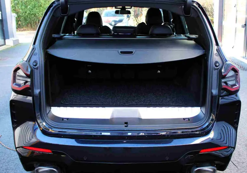 Vue arrière d'un BMW X3 xDrive 30e 2023 bleu métal avec coffre ouvert et banquette arrière visible.