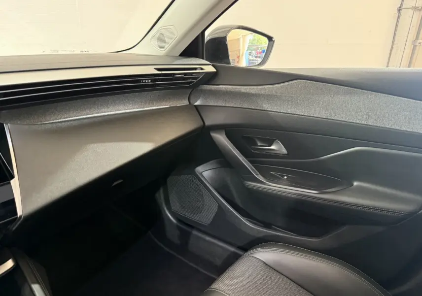 Intérieur côté passager de la Peugeot 308 bleu 2023, montrant la porte, le tableau de bord et siège en cuir noir.