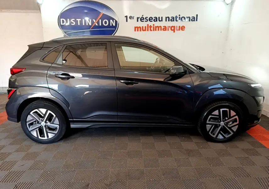 Vue de profil côté gauche d'un Hyundai Kona électrique gris foncé stationné en intérieur avec jantes distinctives.