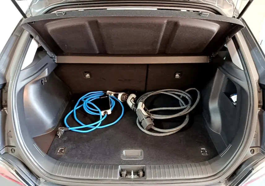 Coffre ouvert d'une Hyundai Kona électrique gris foncé avec câbles de recharge visibles à l'intérieur.