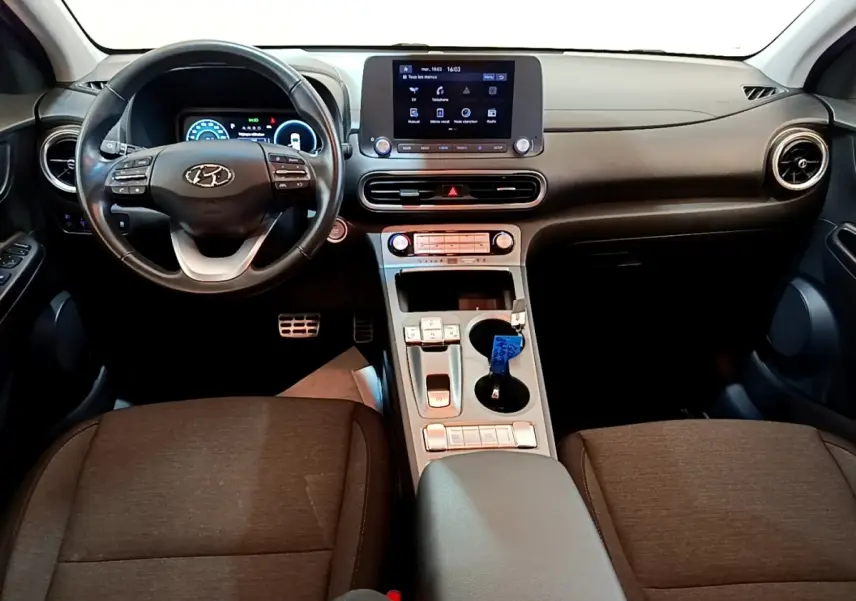 Vue intérieure frontale du tableau de bord et volant cuir noir de la Hyundai Kona électrique avec écran tactile central.