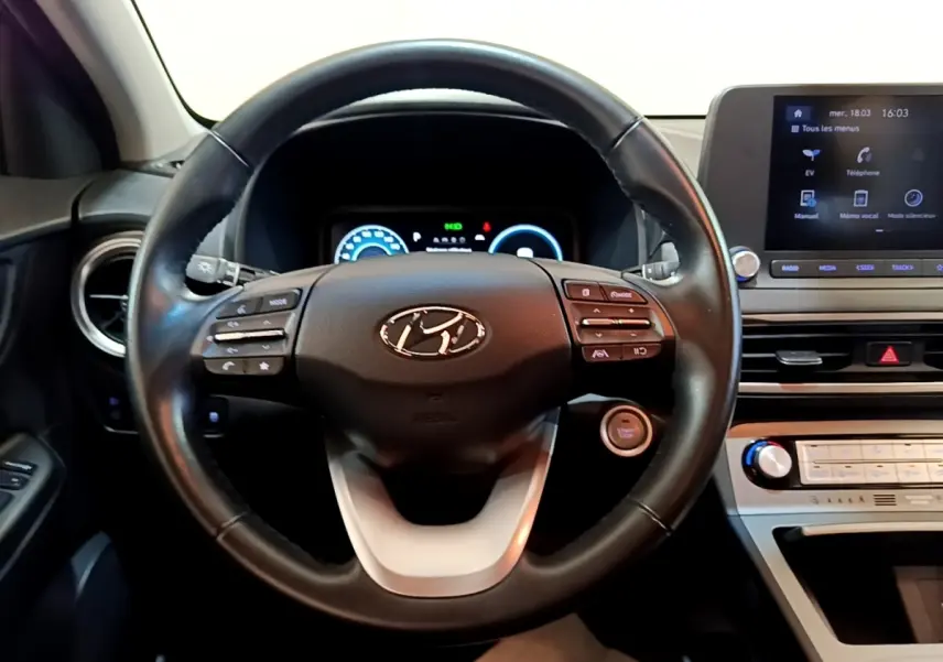 Vue intérieure centrée sur le volant cuir multifonctions noir d’une Hyundai Kona électrique avec tableau de bord digital et écran tactile.