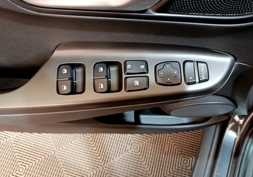 Vue rapprochée des commandes de lève-vitres et rétroviseurs sur la porte côté conducteur d’un Hyundai Kona électrique gris.