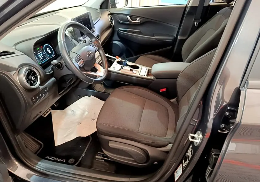 Vue intérieure côté conducteur du Hyundai Kona gris, montrant le volant cuir multifonctions et les sièges tissu foncé.