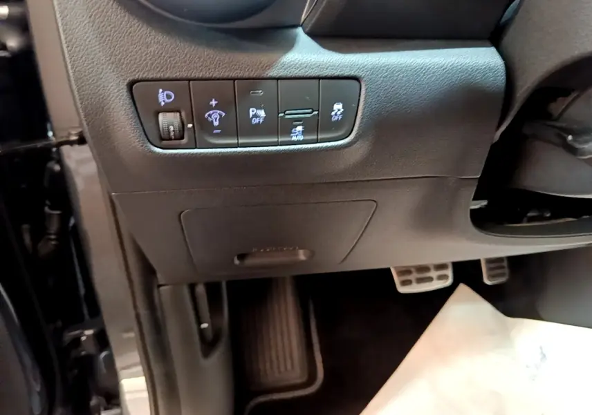 Vue rapprochée côté conducteur du tableau de bord noir avec commandes d’éclairage et aides à la conduite du Hyundai Kona électrique.