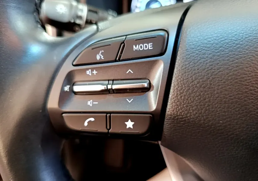 Gros plan sur les commandes du volant cuir multifonctions du Hyundai Kona électrique, boutons de volume et mode visibles.