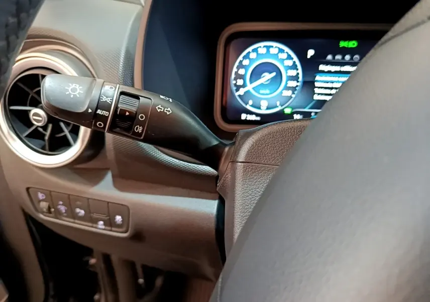 Gros plan sur le commodo gauche et le tableau de bord numérique bleu du Hyundai Kona électrique, intérieur noir.