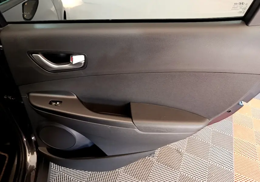 Vue intérieure côté gauche de la porte avant d'une Hyundai Kona électrique 2021 avec garniture noire et poignée argentée.