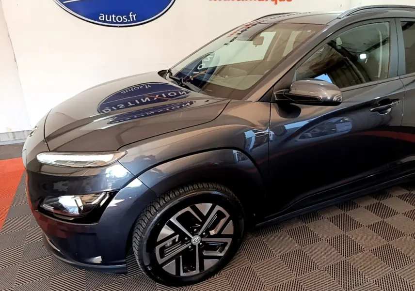 Vue 3/4 avant droit d'une Hyundai Kona électrique gris foncé avec jantes au design moderne et rétroviseurs assortis.