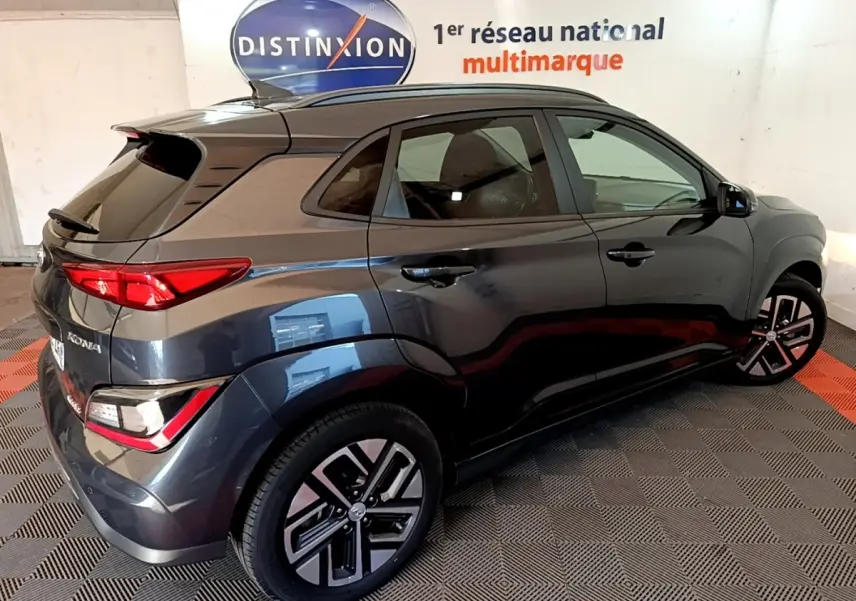 Vue 3/4 arrière droite d'un Hyundai Kona électrique gris foncé avec jantes alliage et toit noir dans un showroom.