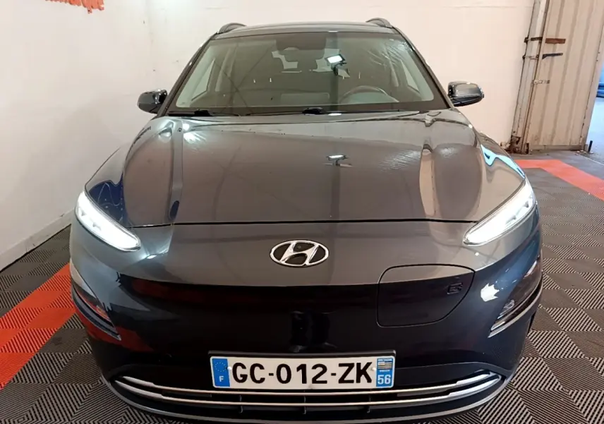 Vue de face d'un Hyundai Kona électrique gris foncé avec phares LED allumés dans un garage.