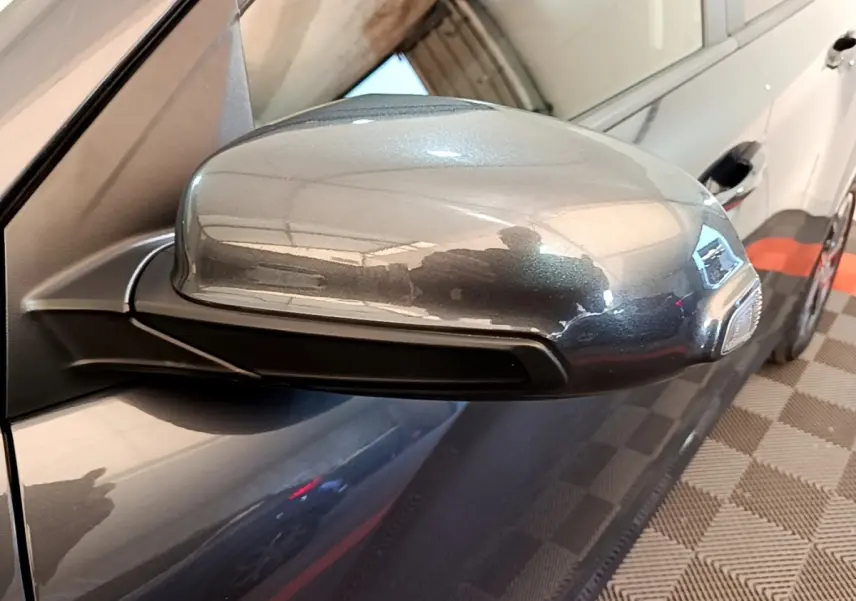 Rétroviseur côté conducteur gris métallisé d'une Hyundai Kona électrique 2021, avec carrosserie sombre visible en arrière-plan.