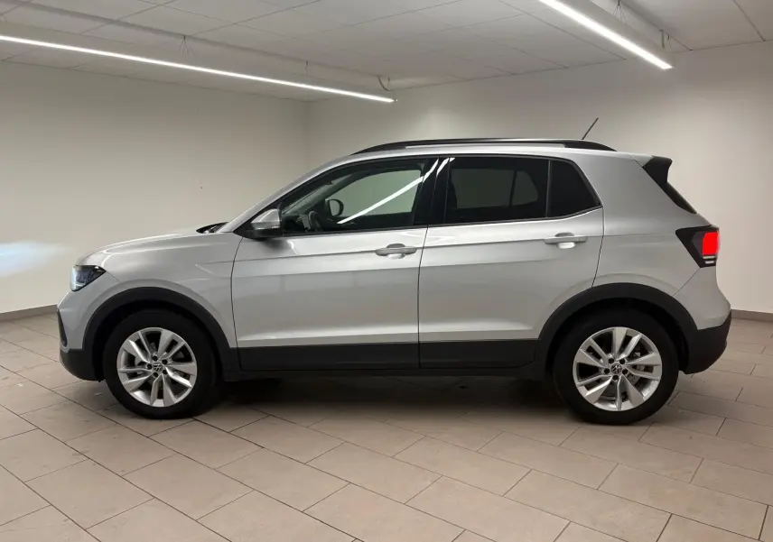 Vue de profil côté gauche d'un Volkswagen T-Cross 2024 en reflet d'argent, avec jantes alliage et vitres surteintées.