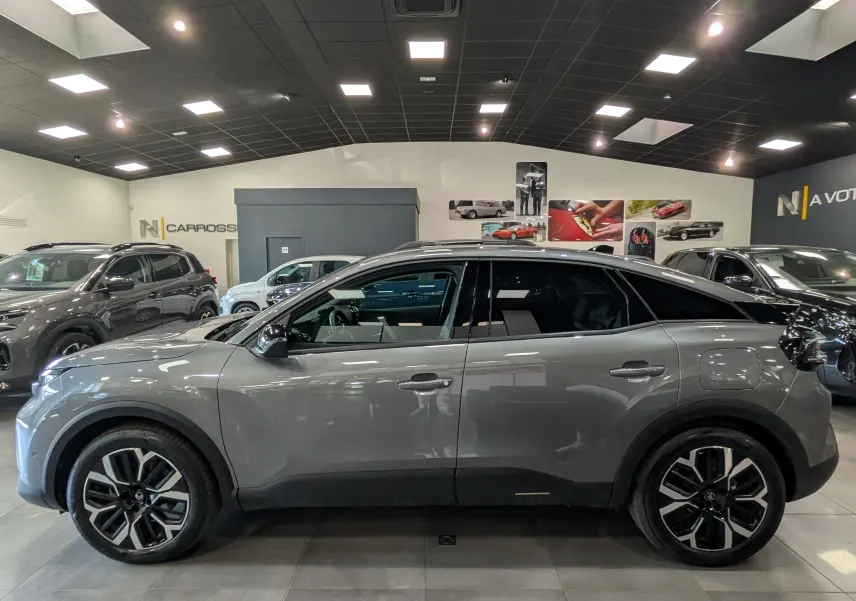 Profil latéral droit d'une Citroën C4 Hybride 145 CH e-DCS6 MAX gris Mercury en showroom, avec jantes biton noires et toit noir.