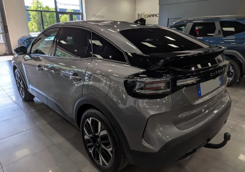 Vue 3/4 arrière droite d'une Citroën C4 hybride gris Mercury avec toit noir et attelage visible en showroom.