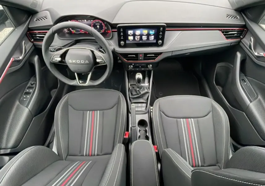 Vue intérieure frontale du Skoda Kamiq Monte Carlo 2026, sièges noirs à bandes rouges et tableau de bord avec écran tactile.