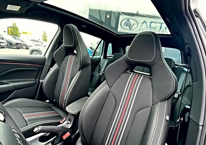 Vue intérieure côté conducteur du Skoda Kamiq blanc nacré 2026, sièges sport noirs avec bandes rouges et toit panoramique.