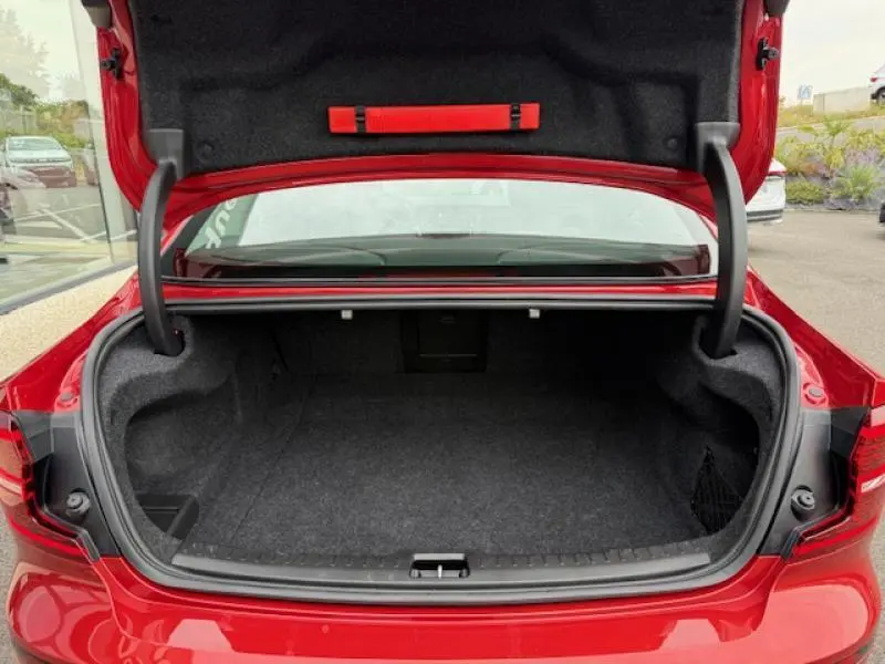 Coffre ouvert vu de l'arrière d'une Volvo S60 2024 rouge fusion métallisé, montrant l'espace de chargement vide.
