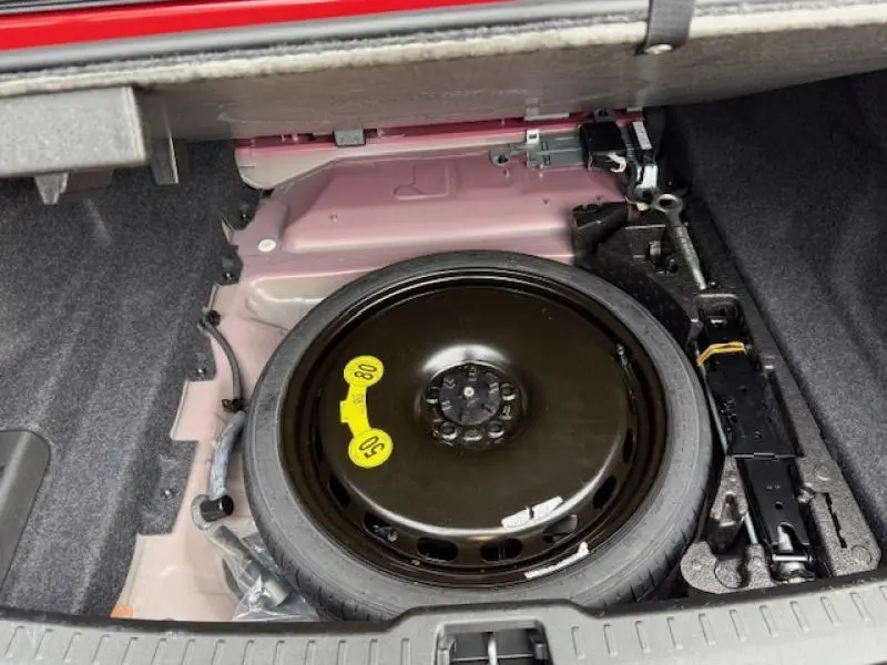 Vue du coffre ouvert d'une Volvo S60 rouge 2024, montrant la roue de secours compacte et les outils de changement de pneu.