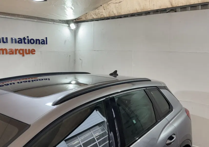 Vue arrière côté gauche d'un Audi Q4 E-TRON gris foncé avec toit panoramique et barres de toit chromées.