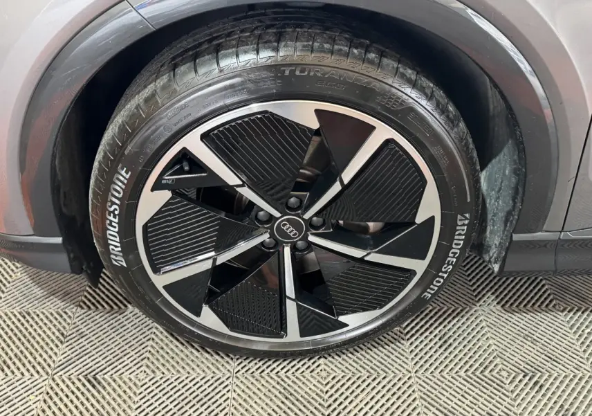 Gros plan sur la roue avant droite d'un Audi Q4 E-TRON gris foncé avec jante noire et argentée au design moderne.