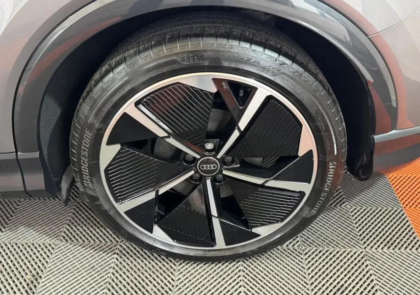 Gros plan sur la roue avant droite de l'Audi Q4 E-TRON gris foncé, jante design noir et argent avec logo Audi central.
