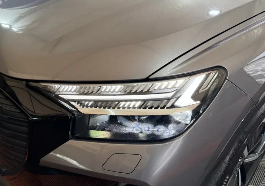 Gros plan sur le phare avant droit allumé d’un Audi Q4 E-TRON gris foncé avec détails LED et calandre noire brillante.