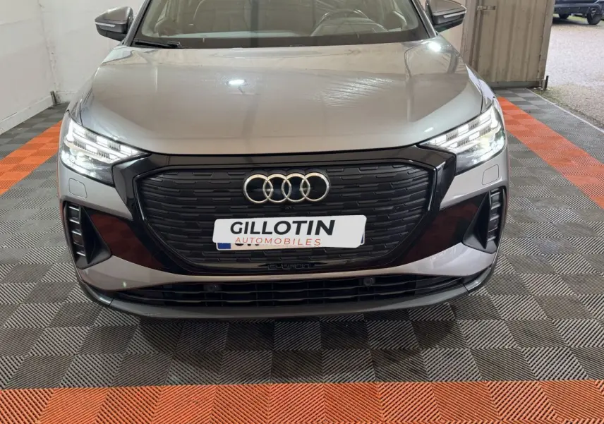 Vue avant d'un Audi Q4 E-TRON gris foncé avec calandre noire et phares LED allumés en intérieur.