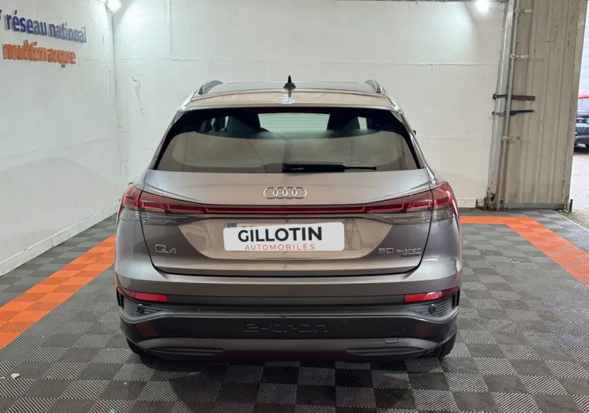 Vue arrière d'un Audi Q4 E-TRON gris foncé avec feux LED reliés et logo e-tron visible sur le pare-chocs.