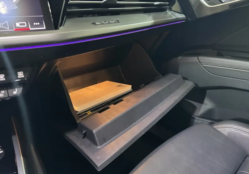 Gros plan sur la boîte à gants ouverte de l'Audi Q4 E-Tron gris foncé, avec éclairage d'ambiance violet visible.