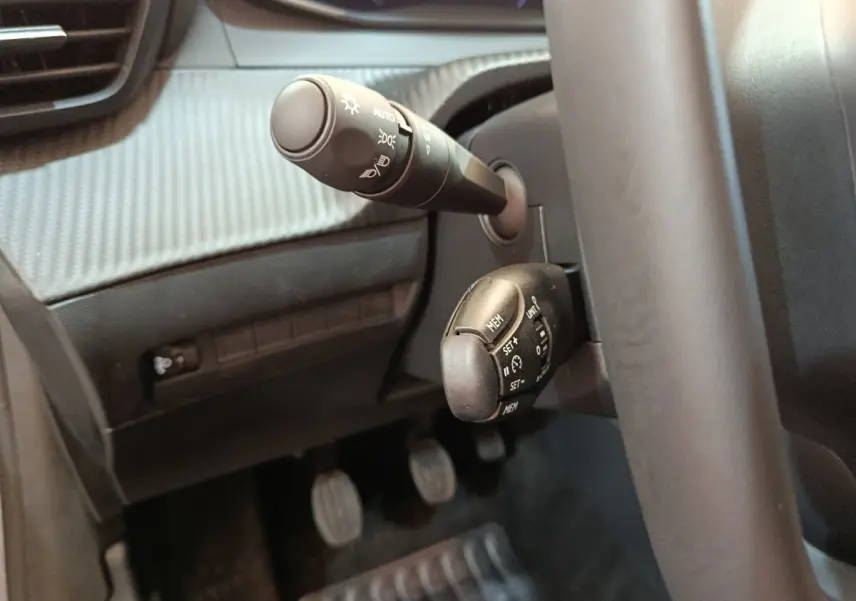 Gros plan sur commandes au volant et levier de clignotant dans l’habitacle gris foncé d’une Peugeot 208 2025.