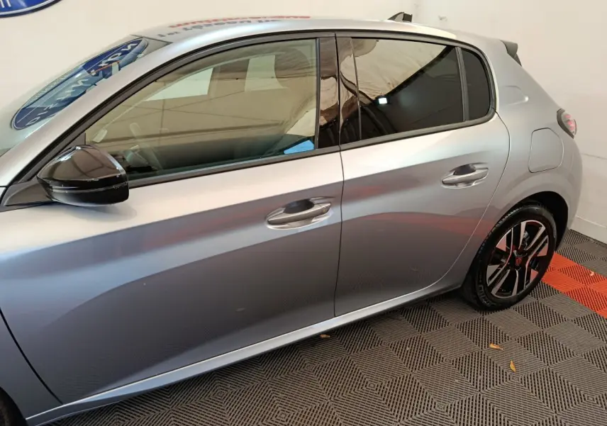 Vue latérale droite d'une Peugeot 208 gris clair avec rétroviseur noir et jantes alliage bicolores.