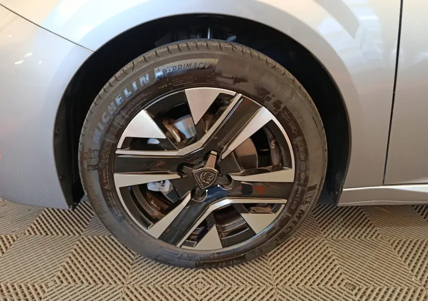 Gros plan sur la roue avant droite gris clair de la Peugeot 208 avec jante alliage noire et argentée au logo lion.