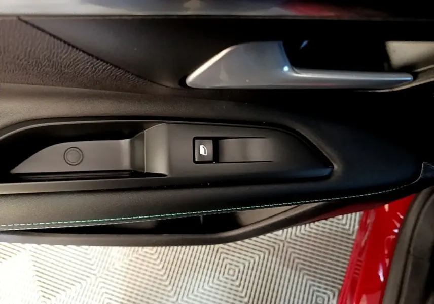Gros plan sur la commande de lève-vitre côté gauche intérieur d'une Peugeot 3008 rouge avec surpiqûres bleues.