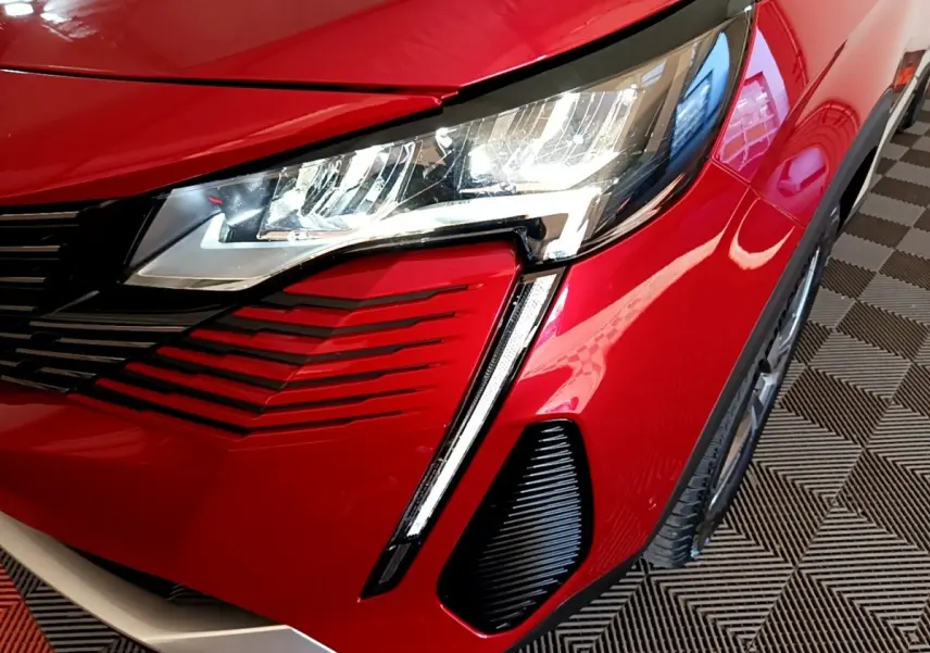 Gros plan sur l'avant droit rouge vif du Peugeot 3008 hybride, mettant en valeur le phare LED et la calandre noire.