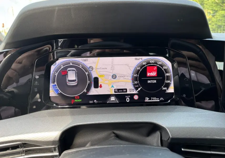 Vue rapprochée du tableau de bord numérique de la Volkswagen Golf blanche 2024, affichant la navigation et la radio.