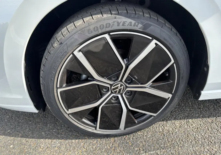 Gros plan sur la roue avant droite d’une Volkswagen Golf blanche 2024 avec jante noire et argentée distinctive.