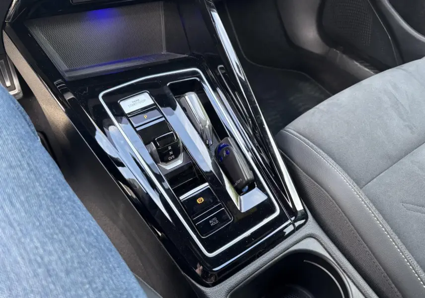 Gros plan sur la console centrale noire brillante de la Volkswagen Golf blanche 2024, avec levier de boîte auto et bouton start/stop.