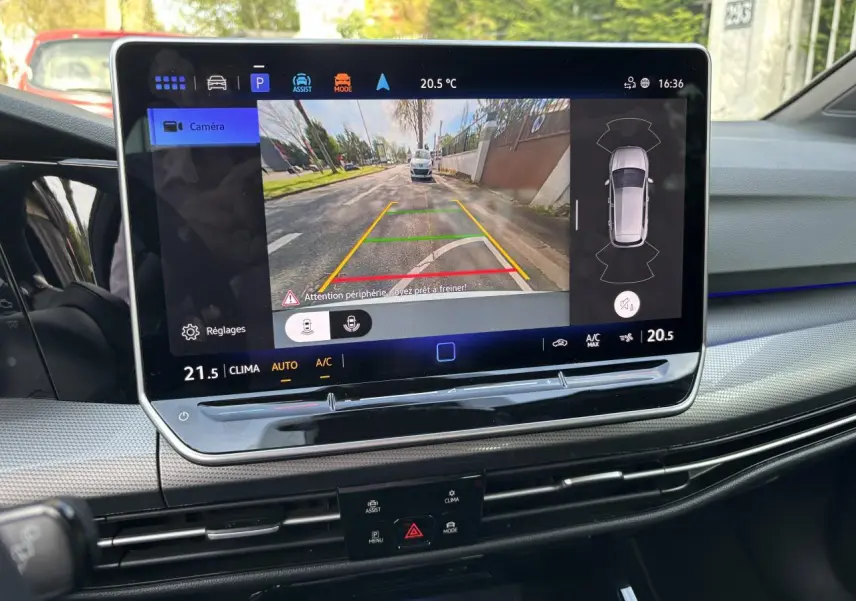 Vue intérieure du tableau de bord de la Volkswagen Golf blanche 2024, écran tactile affichant la caméra de recul et l'aide au stationnement.